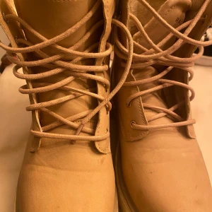 Beige fodrade kängor med snörning - Säljer ett par beige kängor med snörning och mjukt foder på insidan. Skorna har en robust sula och är perfekta för kyligare dagar. Klassisk design med rund tå och dragflik baktill för enkel påtagning.