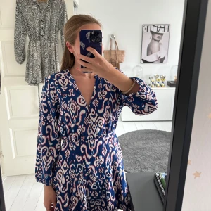 Mönstrad kortklänning med v-ringning - Säljer en kortklänning med vitt, blått och rött mönster. Passar mig perfekt som bär S i kläder vanligtvis. Supersnygg och bekväm att bära!