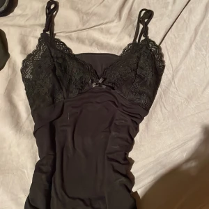 Svart spetsklänning med smala axelband - Säljer en svart klänning med smala axelband och v-ringad spets upptill. Klänningen har en tight passform och är tillverkad i ett mjukt, stretchigt material. Perfekt för dig som gillar en stilren och feminin look.