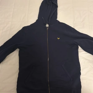 Mörkblå hoodie från Lyle & Scott - Säljer en mörkblå hoodie från Lyle & Scott med dragkedja och huva. Tröjan är ett bra skick och allt funkar som det ska