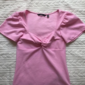 Rosa topp fr Vero Moda - Säljer en söt rosa topp från Vero Moda med korta puffärmar och snygg knutdetalj framtill. Toppen har en djupare urringning och är tillverkad i mjuk bomull. Perfekt för dig som vill ha en feminin och trendig look!💞💞liten i storleken 💞