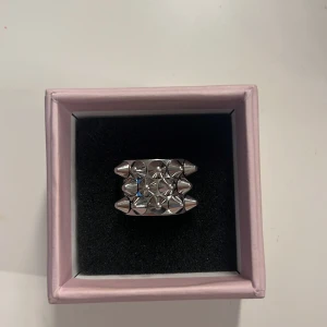 Silvrig Edblad ring med nitar!! - Cool ring i silverfärg med tre rader av pyramidformade nitar. Ringen har en bred design och är perfekt för dig som gillar en edgy stil. Observera att ringen har en liten ”skada” på kanten. (Inget som märks eller känns på insidan när man har på den!!)