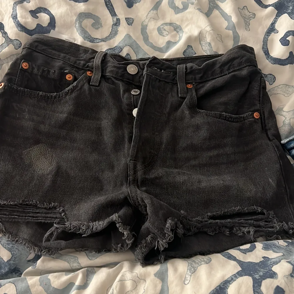 Snygga svarta jeansshorts från Levi's Premium med fransig kant och klassisk femficksdesign. Shortsen har hög midja, knappgylf och slitna detaljer för en cool look. Perfekta för sommaren!. Shortsit.