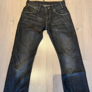 Levi's 523 mörkblå jeans - Mörkblå jeans från Levi's modell 523 med klassiska gula sömmar och femficksdesign. Byxorna har rak passform och normal midja. Knappt använda. Små defekter i högra bakficka