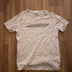 Vit t-shirt från Lindbergh - Vit t-shirt från Lindbergh med svart texttryck på bröstet. Klassisk passform och rund halsringning. Perfekt för en clean och enkel stil.