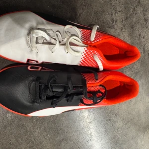 Puma EvoSpeed fotbollsskor i svart, vitt och rött - Aldrig använda bara testade.  Säljer ett par Puma EvoSpeed fotbollsskor med unik design – ena skon är svart och röd, den andra vit och röd. Skorna har snörning och mönstrad sula för bra grepp. Perfekta för dig som vill sticka ut på planen!