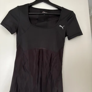Svart sporttopp från Puma - Säljer en svart sporttopp från Puma med rund halsringning och korta ärmar. Toppen är tillverkad i ett stretchigt material med meshdetaljer för extra ventilation. Perfekt för träning och har en diskret Puma-logga på bröstet.