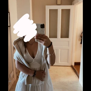 Vit omlottklänning - Säljer en söt vit omlottklänning med korta ärmar och volangdetaljer. Perfekt för sommarens varma dagar. Klänningen har en knytning i midjan för en justerbar passform.