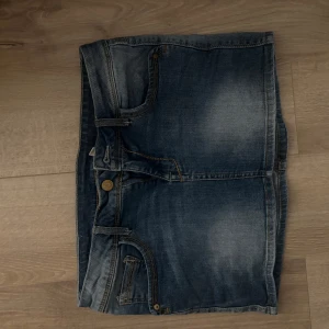 Jeanskjol - Snygg jeanskjol i en klassisk blå denimfärg. Kjolen har en kort längd med femficksdesign och knappstängning fram. Perfekt för en avslappnad stil.