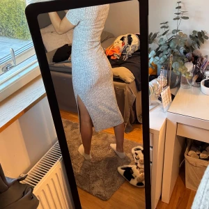 Grå ribbad klänning med slits - Säljer en stilren grå ribbad klänning med korta ärmar och en slits på sidan. Perfekt för en avslappnad men ändå chic look. Klänningen har en tight passform som framhäver figuren.