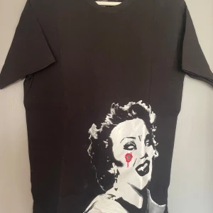 Svart t-shirt med tryck - Cool svart t-shirt med ett unikt tryck av ett ansikte i vitt och rött. Perfekt för dig som vill sticka ut med en edgy stil. Passar bra till jeans eller shorts för en avslappnad look.