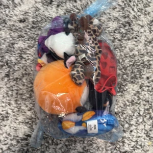 Mystery bag med gosedjur och figurer - En påse fylld med olika små mjukisdjur i varierande färger och mönster. Perfekt för samlare eller som presenter. Innehåller bland annat en orange bollformad figur och en leopardmönstrad figur.