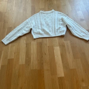 Vit stickad tröja från Gina Tricot - Säljer en snygg vit stickad tröja från Gina Tricot. Tröjan har ett fint flätmönster och är croppad med långa ärmar. Perfekt för kyligare dagar. Passar bra till både jeans och kjol. 🧶✨