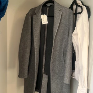 Grå kappa från Pull&Bear - Oanvänd. Snygg grå kappa från Pull&Bear med klassisk design. Stilren look och långa ärmar. Kappan har en enkel knäppning framtill och är tillverkad i ett mjukt material som ger en bekväm passform. 