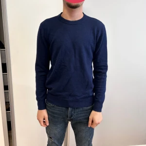 Mörkblå tröja - Säljer en stilren mörkblå tröja med rund halsringning. Tröjan har långa ärmar och ribbade muddar vid ärmslut och nederkant. Perfekt för en avslappnad look.