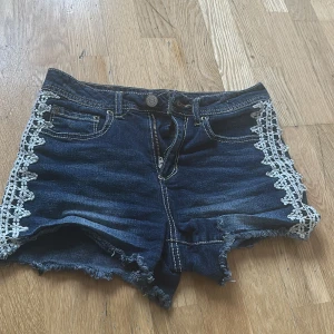 Jeansshorts med spetsdetaljer - Snygga jeansshorts med fransiga kanter och vita spetsdetaljer längs sidorna. Perfekta för sommardagar och ger en cool och avslappnad look. De har en knapp och dragkedja framtill samt klassiska bakfickor.🩷