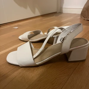 Vita klackskor - Snygga vita sandaler med öppen tå och justerbara remmar. De har en bekväm blockklack som ger extra höjd utan att kompromissa med komforten. Perfekta för sommarens alla tillfällen.