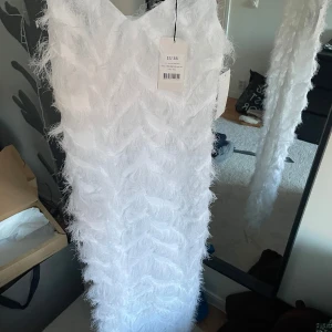 Vit klänning från Josefine HJ x NAKD - Säljer en elegant vit klänning från Josefine HJ x NAKD. Klänningen har en unik fjäderliknande textur och smala axelband. Perfekt för speciella tillfällen där du vill sticka ut. 💫