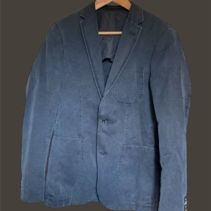 Sand linnekavaj - Snygg blå kavaj med klassisk design och två knappar framtill. Den har långa ärmar och praktiska fickor. Perfekt för en stilren look.