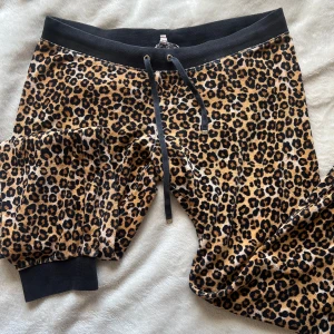 Leopardmönstrade vintage Juicy Couture mjukisbyxor - Snygga leopardmönstrade mjukisbyxor från Juicy Couture med svarta muddar och snörning i midjan. Perfekta för en avslappnad stil med en touch av vildhet. Byxorna har bakfickor med knappar för extra stilpoäng. De är äkta vintage 