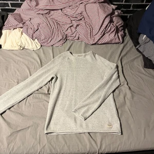 Grå tröja från Jack & Jones - Säljer en stilren grå tröja från Jack & Jones. Tröjan har en enkel design med långa ärmar och är tillverkad i ett mjukt material. Perfekt för en avslappnad look., finns en fläck på högerarm ( går att tvätta)