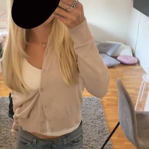 Beige kofta - Säljer en stilren beige kofta med knappar framtill. Koftan har långa ärmar och en mjuk, bekväm passform. Perfekt för lager-på-lager-stil och passar till många olika outfits.
