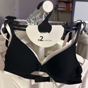 Svart och vit t-shirt bh från Lindex - Säljer ett set med två t-shirt bh:ar från Lindex i storlek 65A. En i klassisk svart och en i stilren vit. Perfekta för vardagsbruk med bekväm passform och släta kupor. Passar under alla typer av kläder för en osynlig look.