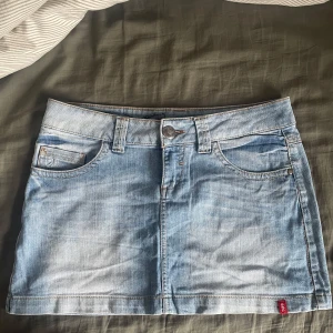 Ljusblå jeanskjol - Snygg ljusblå jeanskjol med klassisk femficksdesign och knappstängning fram. Perfekt för en avslappnad stil. Den har en kort längd och är tillverkad i ett slitstarkt denimtyg.