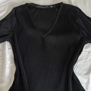 Svart ribbad topp från The Black Label Collection  - Snygg svart ribbad topp från The Black Label Collection med v-ringning. Den är knappt använd och är ifrån lager 157