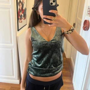 Grön sammetstopp - Snygg grön sammetstopp med v-ringning. Toppen är ärmlös och har en mjuk, glansig yta som ger en lyxig känsla. Perfekt för att klä upp en outfit med lite extra stil.