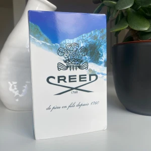 Creed Silver Mountain Water Parfym - Säljer en exklusiv Creed Silver Mountain Water parfym. Flaskan är vit med en elegant silverfärgad kork och rymmer 120 ml. Förpackningen har en vacker design med snöklädda berg, vilket speglar doftens friska och rena karaktär. Perfekt för den som söker en lyxig och uppfriskande doftupplevelse.