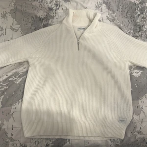 Vit stickad tröja från Jack & Jones - Säljer en stilren vit stickad tröja från Jack & Jones. Tröjan har en dragkedja vid halsen och ribbade detaljer. Perfekt för kyligare dagar. Passar väldigt bra till jeans. Den har en liten fläck inne i tröjan.