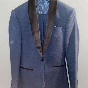 Blå kavaj med svarta slag och matchande byxor - Elegant blå kavaj med svarta slag och blommigt foder från Isaac Dewhirst. Matchande byxor i samma blå nyans. Perfekt för formella tillfällen. Storlek 42. Köpt för 1500kr säljer för 850kr. Har använt den 1 gång 