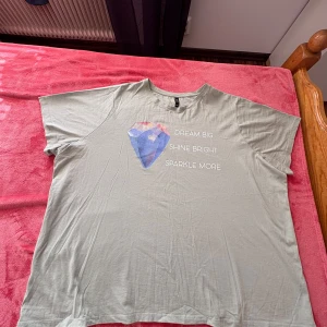 Grön t-shirt med tryck från H&M - Säljer en grön t-shirt från H&M med ett färgglatt diamanttryck och texten 'Dream Big, Shine Bright, Sparkle More'. T-shirten har en avslappnad passform och korta ärmar. Perfekt för en avslappnad stil.