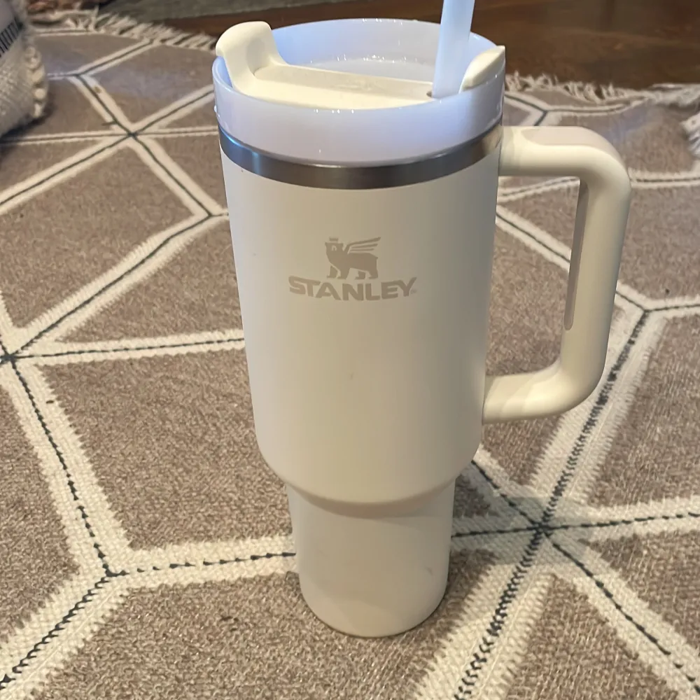 Säljer en stilren vit termosmugg från Stanley med handtag och sugrör. Perfekt för att hålla drycker varma eller kalla under dagen. Muggen har en kapacitet på 40 oz/1,1 L och är idealisk för både vardag och äventyr.. Muu.