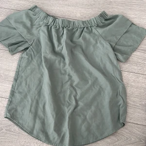 Grön offshoulder topp från H&M - Säljer en stilren grön offshoulder topp från H&M. Toppen har korta ärmar och en elastisk kant mot runt axlarna för en bekväm passform. Perfekt för en avslappnad look. 🌿