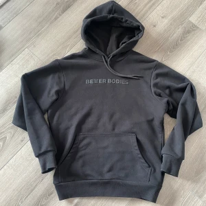 Svart hoodie från Better Bodies - Säljer en svart hoodie från Better Bodies med en stor ficka framtill och justerbar huva. Perfekt för en avslappnad stil eller träning. Texten 'Better Bodies' är tryckt på bröstet. Nypris 999:-