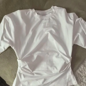Vit t-shirt - Säljer en klassisk vit t-shirt med normal passform. Perfekt basplagg för alla tillfällen. T-shirten har korta ärmar och är tillverkad i mjukt material för extra komfort.