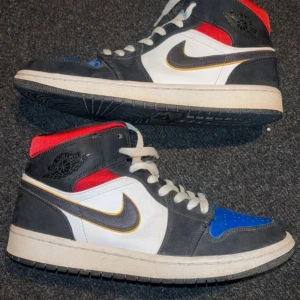 Nike Air Jordans  - Snygga Nike Air Jordans med en mix av färger: svart, vit, röd och blå. Skorna har en klassisk hög design med snörning och den ikoniska Nike-loggan på sidan. 