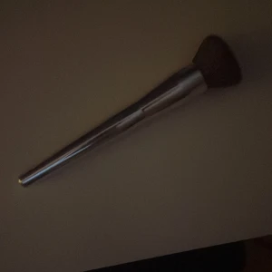 Sminkborste från CAIA - Snygg sminkborste från CAIA med ett silverfärgat handtag och täta, mjuka borst. Perfekt för att applicera puder eller foundation jämnt över ansiktet. Borsten är märkt med 'F14'.