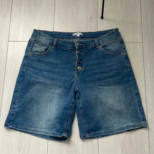 Blå jeansshorts från Sincerely Love - Snygga blå jeansshorts från Sincerely Love med klassisk femficksdesign och knappgylf. Perfekta för en avslappnad stil under varma dagar. De har en bekväm passform och är tillverkade i slitstarkt denim.