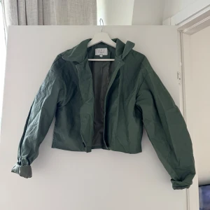 Grön jacka från AFJ x NA-KD - Snygg grön jacka från AFJ x NA-KD med knappar framtill. Jackan har en croppad design och långa ärmar, perfekt för vår och höst. 