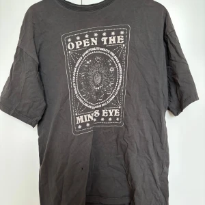 Grå t-shirt med tryck från Even&Odd - Säljer en grå t-shirt från Even&Odd i storlek S men skulle säga att den sitter mer som M med ett coolt tryck på framsidan som säger 'Open the Mind's Eye'. Har ett litet hål på framsidan men inget man tänker på.