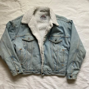 Jeansjacka med teddyfoder från Levi's - Säljer en vintage ljusblå jeansjacka från Levi's med vitt teddytyg inuti. Jackan har en fläck på ena armen som syns på bilden. Ganska står passform, går mot L