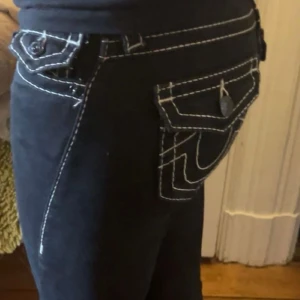 Svarta jeans från True Religion - Snygga svarta jeans från True Religion med vita sömmar. Modellen är midwaist och straight, inte skinny! Har haft ca ett år, köpta på jeans Uno för 1699kr! Säljer då de blivit för små!💕