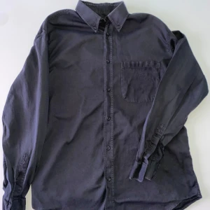 Morkgrå långärmad skjorta från Armani Jeans - Säljer en stilren morkgrå långärmad skjorta från Armani Jeans. Skjortan har en klassisk krage och en bröstficka med knapp. Perfekt för en elegant look.