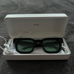 Svarta solglasögon från Chimi - Snygga svarta solglasögon från Chimi med en klassisk fyrkantig form. De har mörka linser och kommer i ett stilrent vitt fodral. Perfekta för att ge en cool touch till din outfit. Modellen 04. 