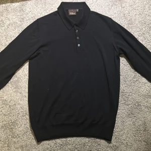 Mörkblå pikétröja  Oscar Jacobson - Snygg mörklbå pikétröja från Oscar Jacobson, tillverkad i Italien. Tröjan har långa ärmar och en klassisk krage med knappar framtill. Perfekt för en stilren look. Tröjan är 100% merino ull. Köpt för 1900. Priset är ej hugget i sten.