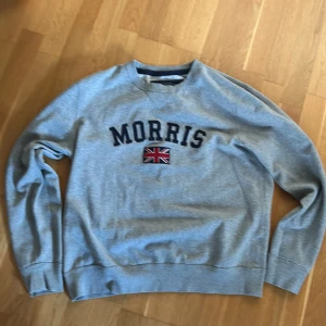 Grå sweatshirt från Morris - Säljer en stilren grå sweatshirt från Morris med text och en brittisk flagga på bröstet💯Tröjan har långa ärmar och ribbade muddar vid ärmslut och nederkant. Perfekt för en avslappnad stil✅ Tröjan är storlek large men den passar lite mindre i storlek så ungefär 📐 bara att skriva om ni har några frågor😊