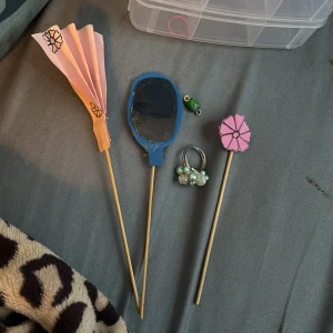 Sommar set: ring, spegel, solfjäder, blomma och berlock  - Ett hemmagjort sommar set innehållande en ring klädd i blåa och vita pärlor. En spegel gjord i foampapper och gamla typ ”lek” solglasögon, en grön, lila, guld (inte äckta) och ljusblå berlock gjord i lera. Och en rosa blomma i rosa foam papper ritad på me svart tuschpenna. Och även sist men inte minst en rosa solfjäder i vanligt färgat papper ritad på med en svart fineliner.
